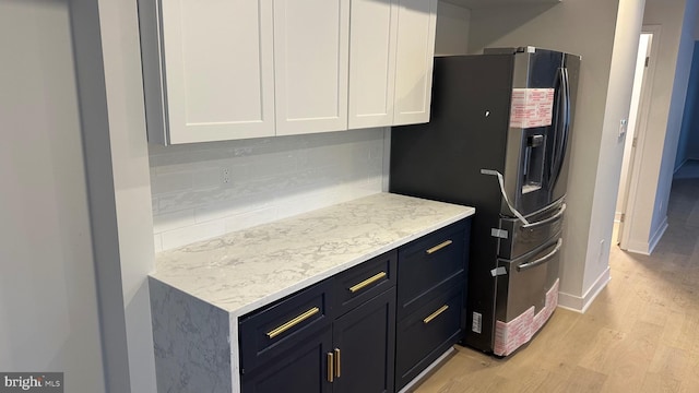 kitchen featuring white cabinets, light wood-type flooring, stainless steel fridge with ice dispenser, and light stone counters