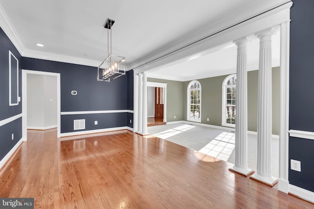 unfurnished dining area with ornate columns, a chandelier, crown molding, and light hardwood / wood-style floors