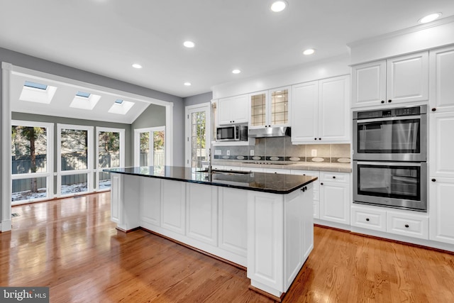 kitchen featuring a center island with sink, appliances with stainless steel finishes, decorative backsplash, vaulted ceiling with skylight, and white cabinets