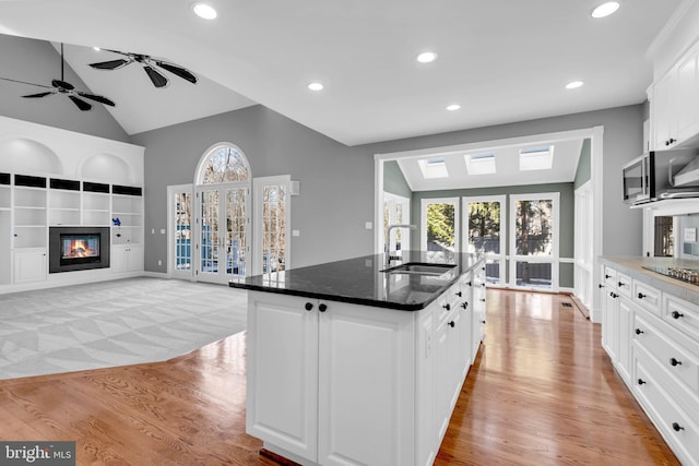 kitchen with white cabinetry, light hardwood / wood-style floors, an island with sink, sink, and built in shelves