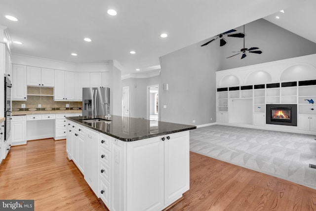 kitchen with dark stone countertops, a center island, white cabinetry, stainless steel fridge with ice dispenser, and high vaulted ceiling