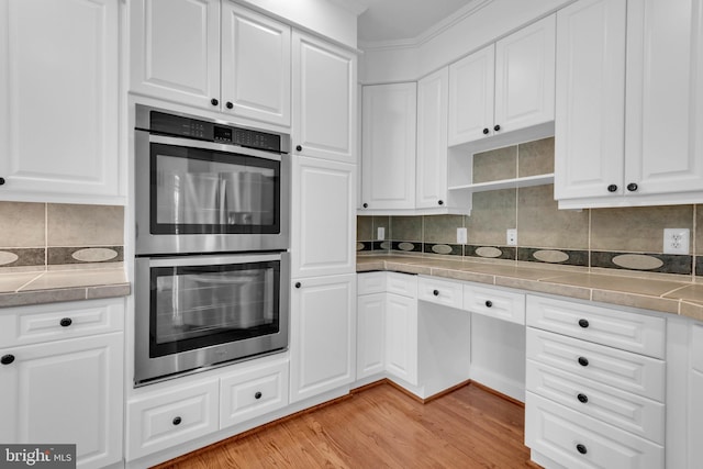 kitchen with white cabinetry, light hardwood / wood-style floors, stainless steel double oven, and backsplash