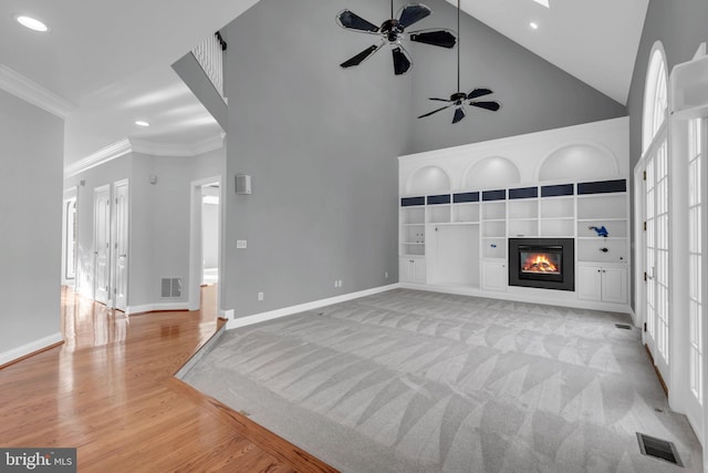 living room with light carpet, ceiling fan, built in features, a towering ceiling, and crown molding