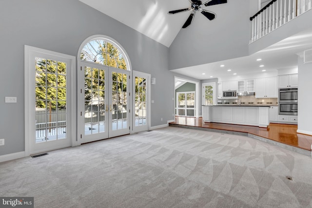 unfurnished living room featuring high vaulted ceiling, light colored carpet, french doors, and a healthy amount of sunlight