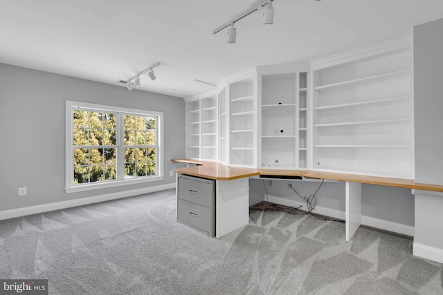 unfurnished office with built in desk, light colored carpet, and rail lighting