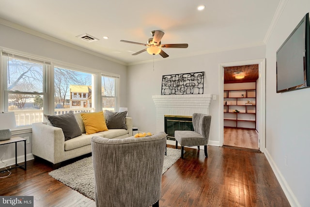 living room with a brick fireplace, ceiling fan, crown molding, and dark hardwood / wood-style flooring