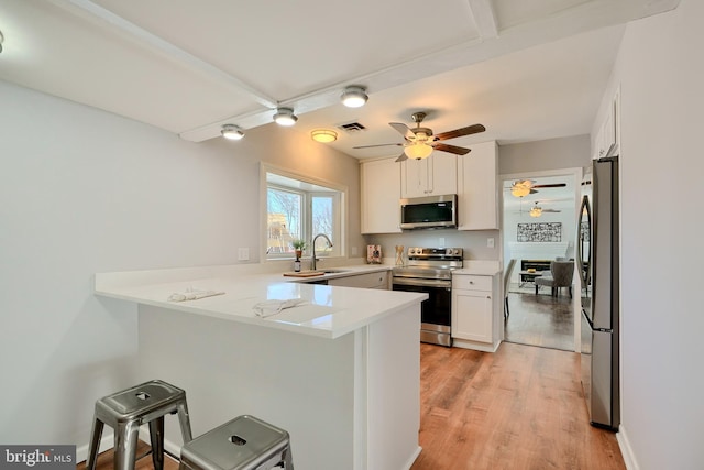 kitchen featuring kitchen peninsula, stainless steel appliances, white cabinets, a kitchen breakfast bar, and sink