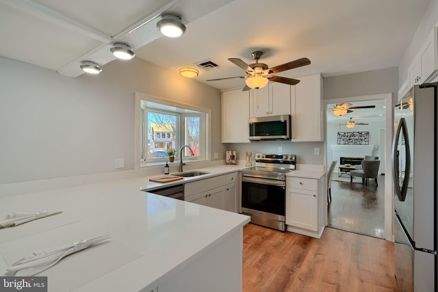 kitchen with stainless steel appliances, sink, white cabinetry, light hardwood / wood-style floors, and kitchen peninsula