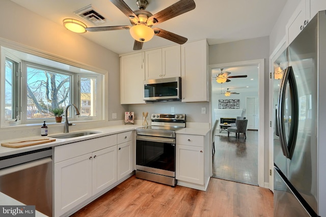 kitchen with stainless steel appliances, white cabinets, sink, and light wood-type flooring