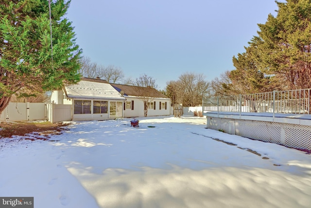 snow covered rear of property featuring a deck and a sunroom