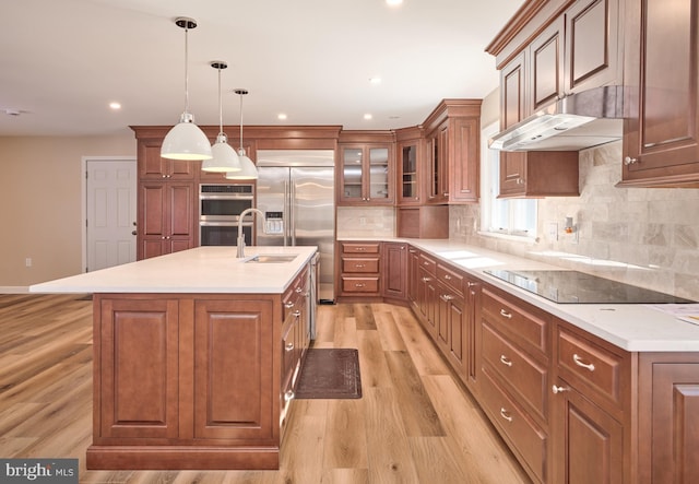 kitchen with sink, hanging light fixtures, backsplash, an island with sink, and appliances with stainless steel finishes