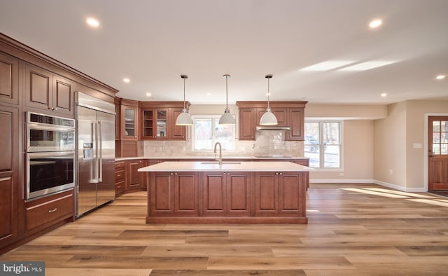 kitchen with hanging light fixtures, sink, an island with sink, appliances with stainless steel finishes, and tasteful backsplash