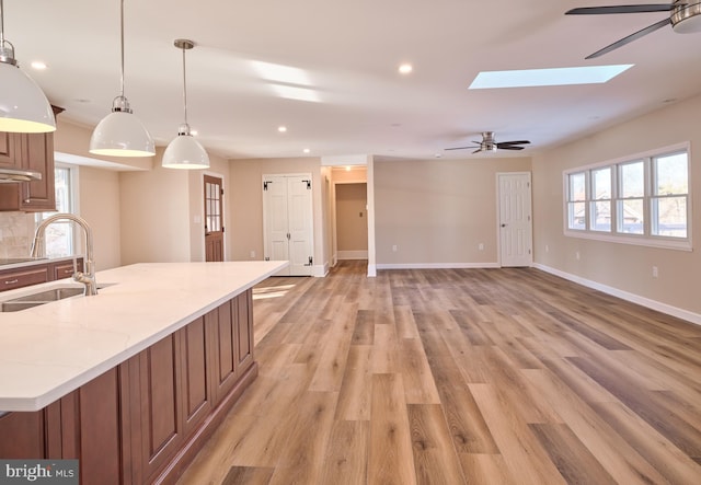 kitchen featuring a skylight, ceiling fan, sink, hanging light fixtures, and light hardwood / wood-style flooring