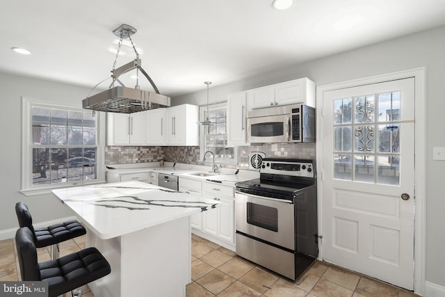 kitchen with appliances with stainless steel finishes, a center island, decorative light fixtures, white cabinetry, and backsplash