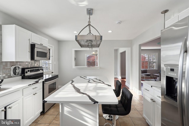 kitchen with light tile patterned floors, stainless steel appliances, hanging light fixtures, a kitchen island, and white cabinets