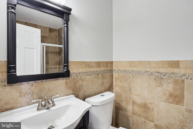 bathroom with toilet, tile walls, sink, and a shower with shower door