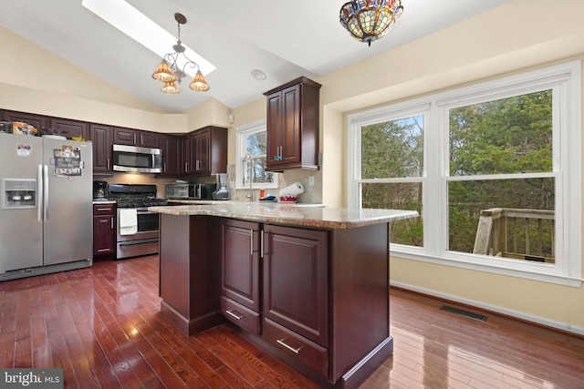 kitchen with hanging light fixtures, vaulted ceiling, appliances with stainless steel finishes, plenty of natural light, and light stone counters