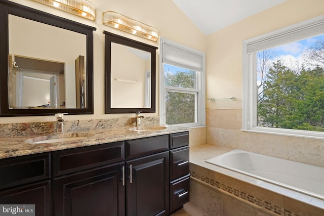 bathroom featuring vanity, vaulted ceiling, plenty of natural light, and tiled tub