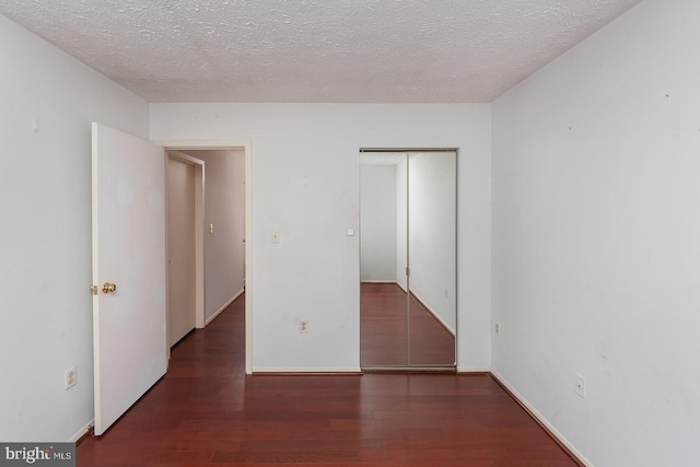 unfurnished bedroom featuring a textured ceiling, dark hardwood / wood-style flooring, and a closet