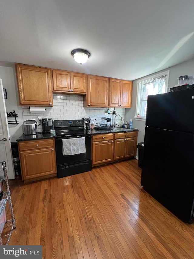 kitchen featuring decorative backsplash, sink, black appliances, and light wood-type flooring