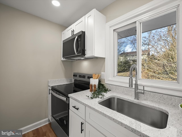 kitchen with electric stove, light stone counters, plenty of natural light, white cabinets, and sink