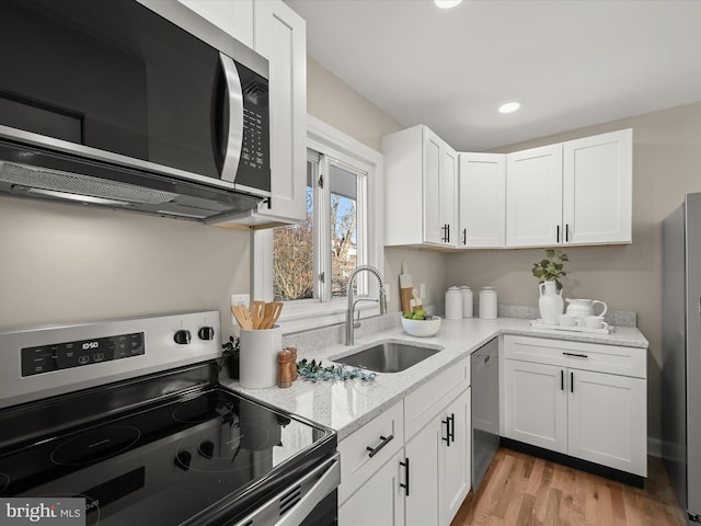 kitchen with stainless steel appliances, sink, white cabinetry, light hardwood / wood-style flooring, and light stone countertops