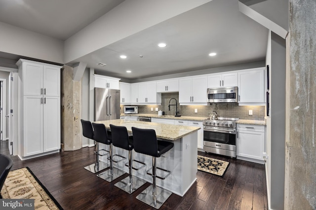 kitchen with light stone countertops, stainless steel appliances, sink, white cabinets, and a center island