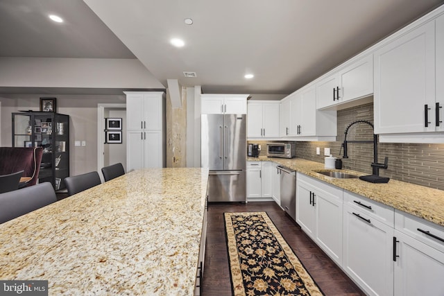 kitchen with a kitchen breakfast bar, light stone counters, white cabinets, and appliances with stainless steel finishes