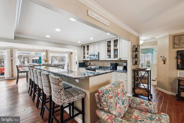 kitchen with a kitchen breakfast bar, white cabinets, dark stone counters, and appliances with stainless steel finishes