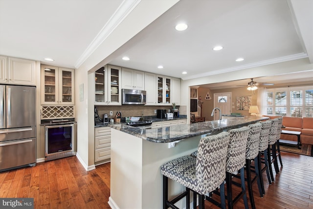 kitchen with appliances with stainless steel finishes, dark stone countertops, a breakfast bar, backsplash, and beverage cooler