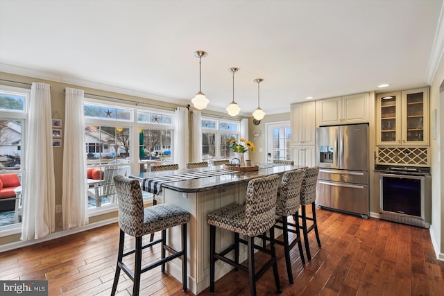 kitchen with stainless steel fridge, hanging light fixtures, dark hardwood / wood-style flooring, a breakfast bar, and ornamental molding