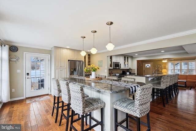 kitchen featuring crown molding, dark stone counters, decorative light fixtures, stainless steel appliances, and a breakfast bar area