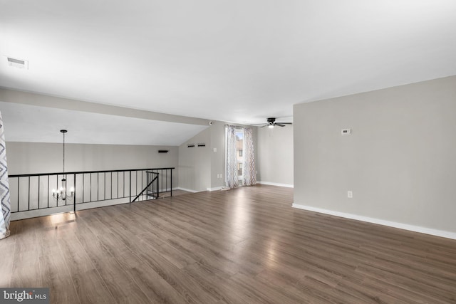 empty room with vaulted ceiling, dark wood-type flooring, and ceiling fan with notable chandelier