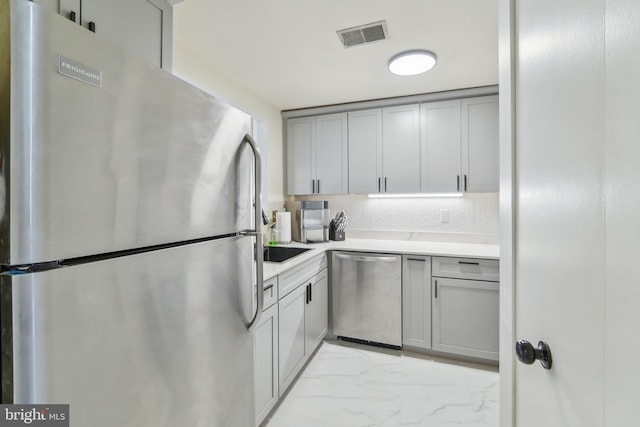 kitchen featuring appliances with stainless steel finishes, gray cabinets, and tasteful backsplash