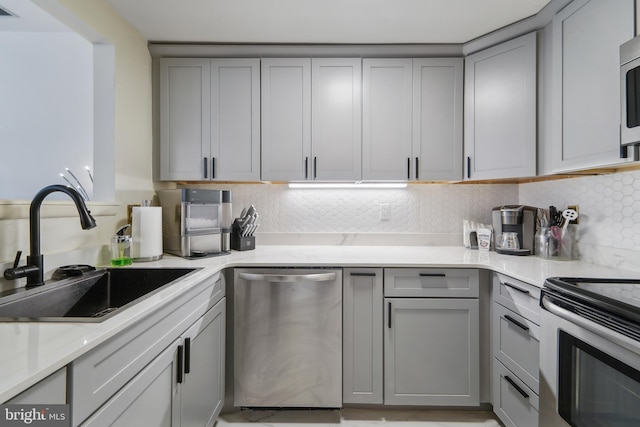 kitchen with sink, decorative backsplash, gray cabinetry, and stainless steel appliances