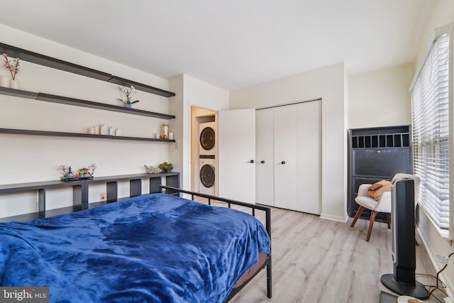 bedroom with a closet, light hardwood / wood-style floors, and stacked washer and dryer