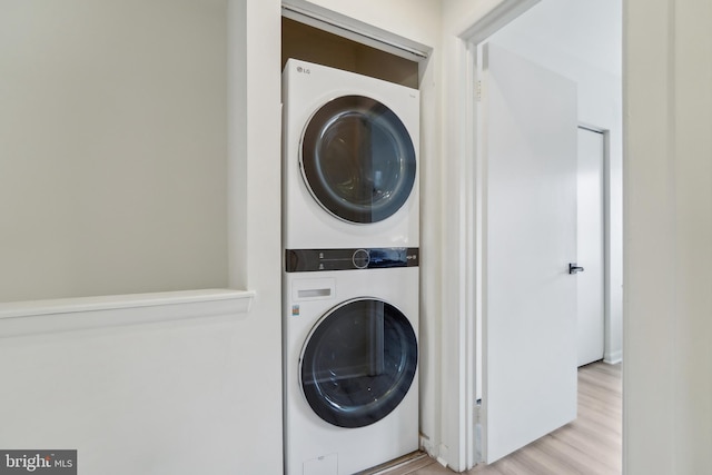 washroom with light hardwood / wood-style floors and stacked washing maching and dryer