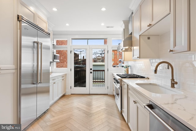 kitchen with ventilation hood, sink, premium appliances, light parquet floors, and light stone counters