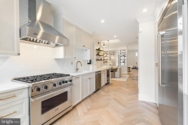 kitchen featuring sink, high end appliances, wall chimney range hood, light stone countertops, and white cabinets