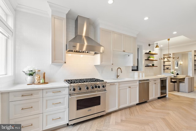 kitchen featuring sink, wine cooler, high end stove, decorative light fixtures, and wall chimney exhaust hood