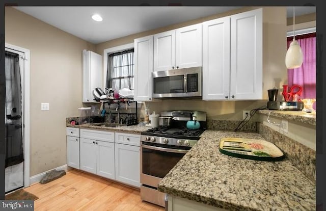 kitchen with appliances with stainless steel finishes, sink, white cabinets, light stone countertops, and light wood-type flooring