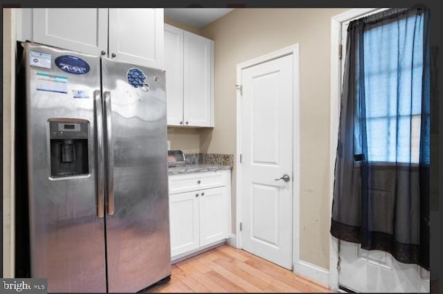 kitchen featuring light stone counters, stainless steel fridge, white cabinets, and light wood-type flooring