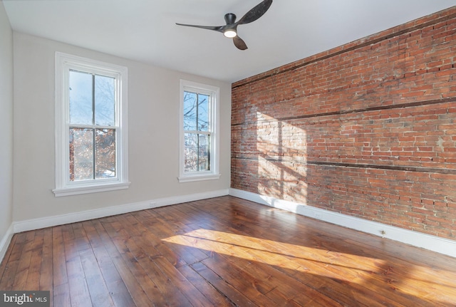 spare room featuring hardwood / wood-style floors, ceiling fan, and brick wall