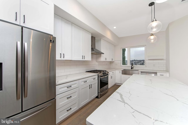 kitchen featuring appliances with stainless steel finishes, pendant lighting, wall chimney exhaust hood, white cabinets, and sink