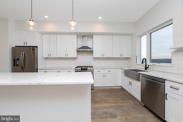 kitchen featuring stainless steel appliances, light stone counters, wall chimney exhaust hood, sink, and white cabinetry