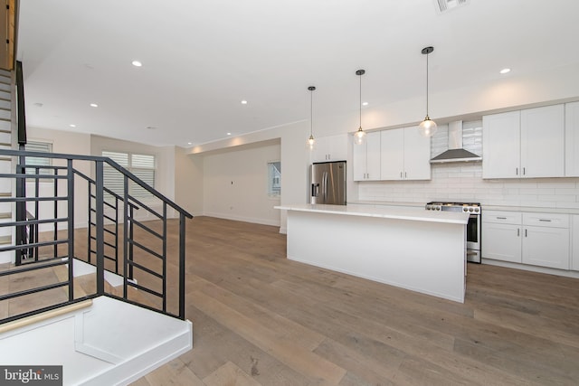 kitchen with stainless steel appliances, wall chimney range hood, tasteful backsplash, a kitchen island, and white cabinets