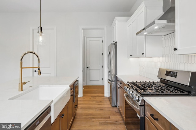 kitchen with white cabinets, appliances with stainless steel finishes, pendant lighting, and wall chimney range hood