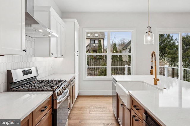 kitchen featuring appliances with stainless steel finishes, wall chimney exhaust hood, pendant lighting, light hardwood / wood-style flooring, and white cabinetry