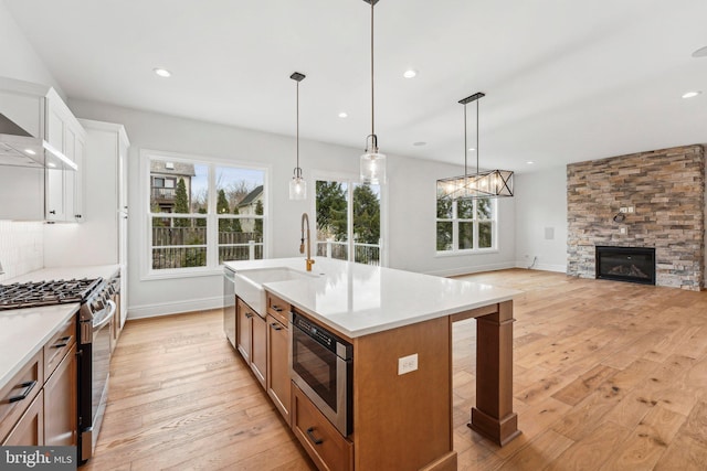 kitchen featuring appliances with stainless steel finishes, a kitchen island with sink, sink, decorative light fixtures, and white cabinetry