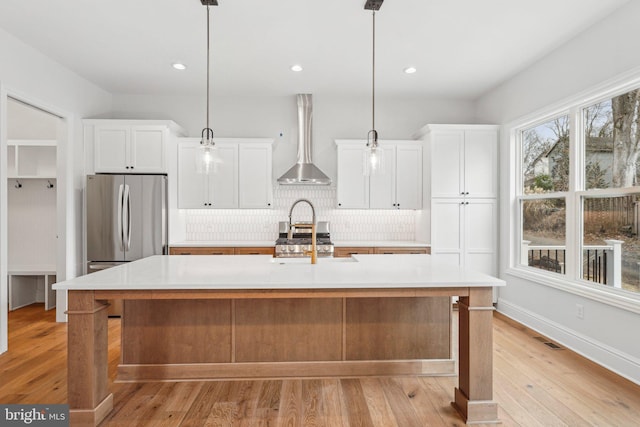 kitchen with decorative light fixtures, white cabinetry, wall chimney range hood, and an island with sink